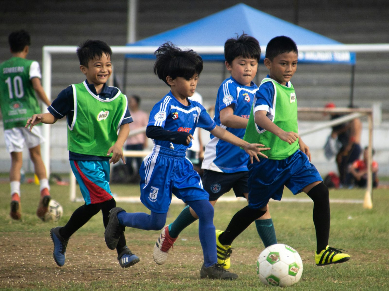 Children in blue football kits and green bibs playing football outdoors